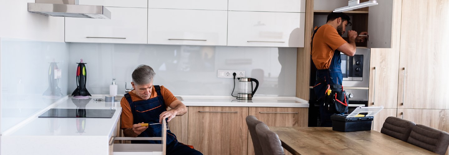 Two contractors installing new kitchen cabinets and drawers, adding the final touches to a new kitchen.