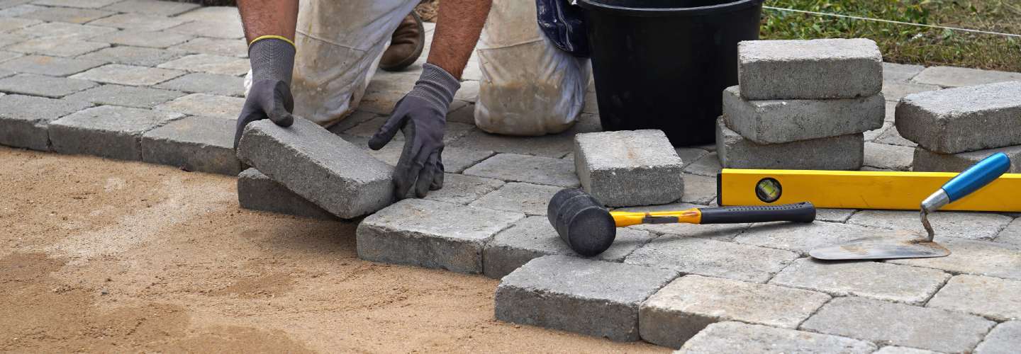 A close up photo of a person paving a patio.