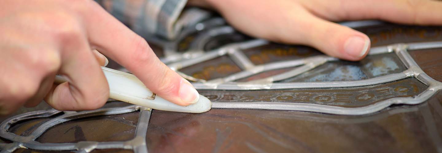 A close-up view of a person repairing a leaded glass window, carefully soldering the intricate pieces together.