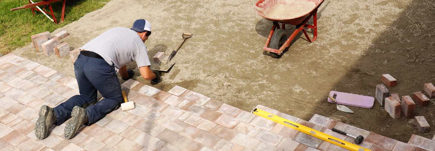 A person installing pavers on a patio, carefully arranging them in a pattern to create a beautiful outdoor space.