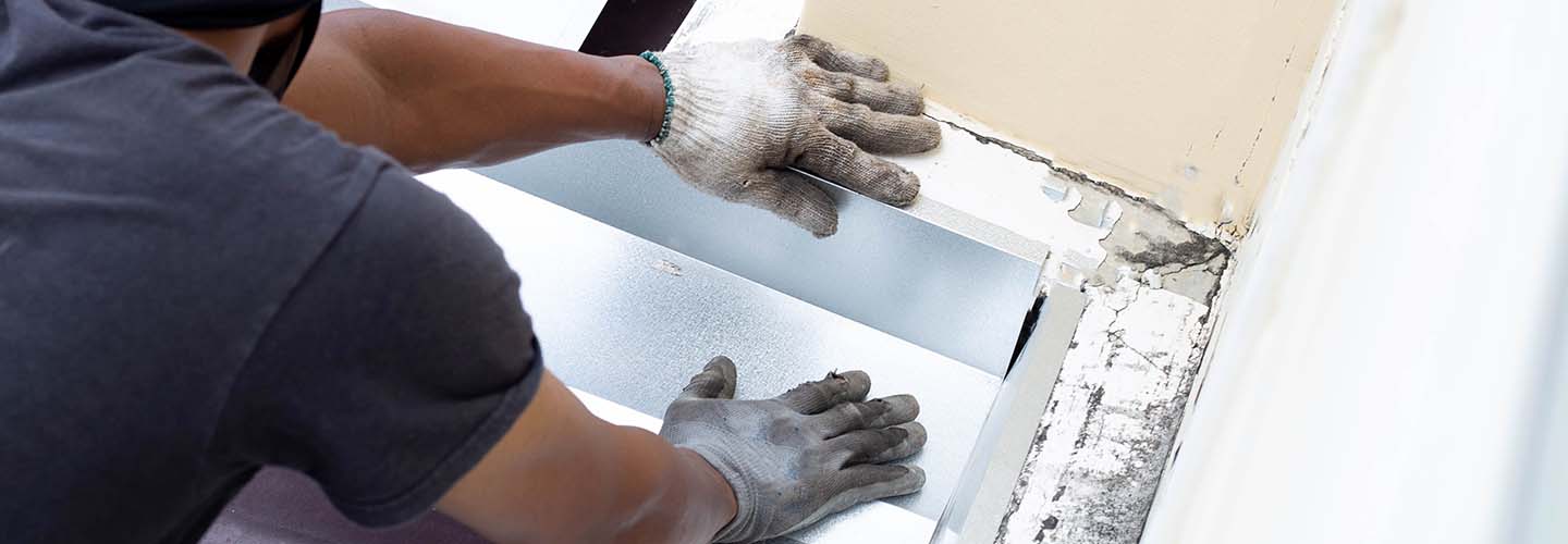 A person repairing water damage on a wall, using tools and wearing protective gear.