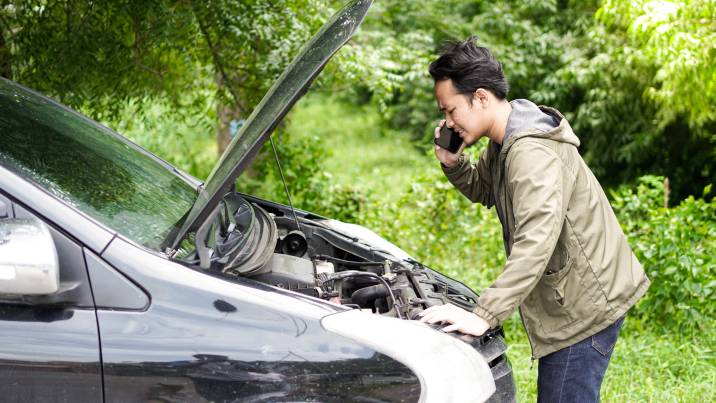 A man with a broken car talking to a mobile mechanic on the phone