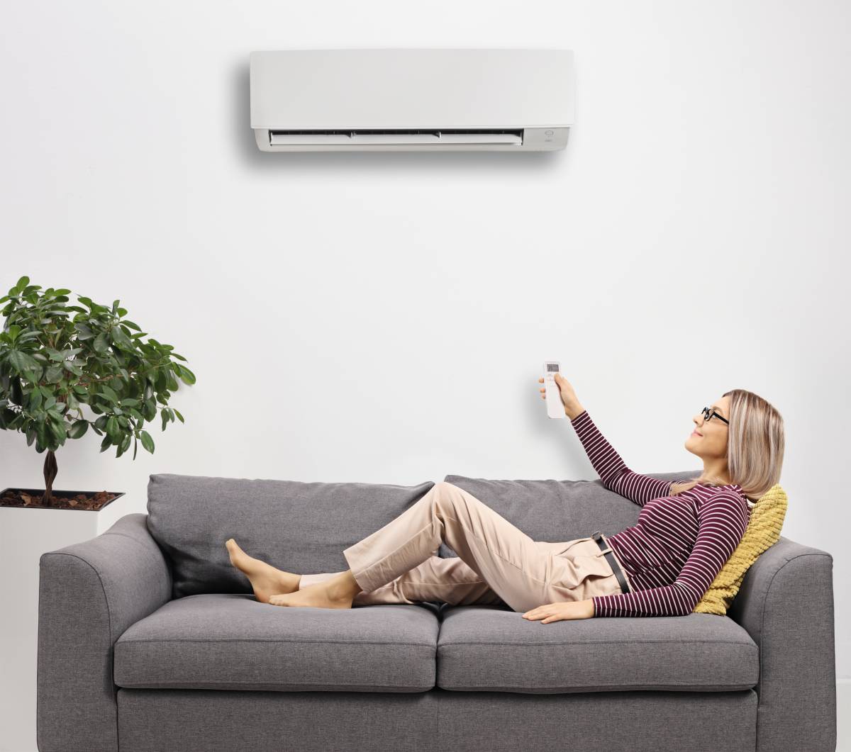 Woman lying down in couch adjusting temperature of air conditioner