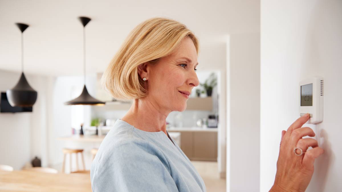 Senior blonde woman adjusting termperature in thermostat