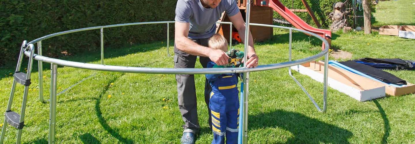 A person assembling a trampoline, with metal frames and springs laid out on the ground, ready to be put together.