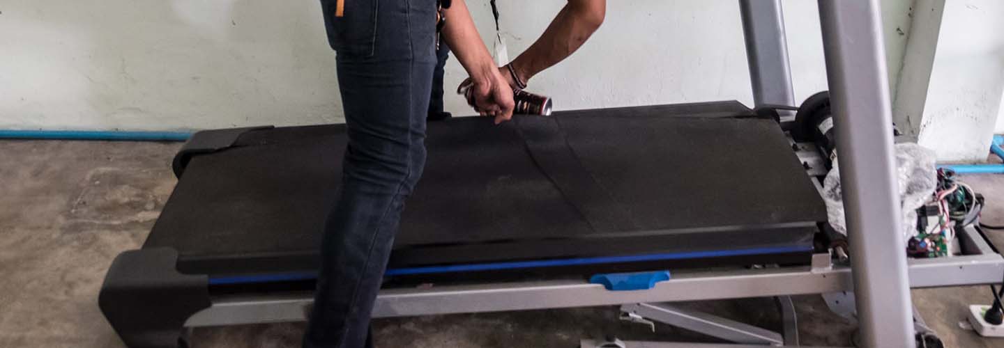 A person assembling a treadmill with tools and parts spread out on the floor.
