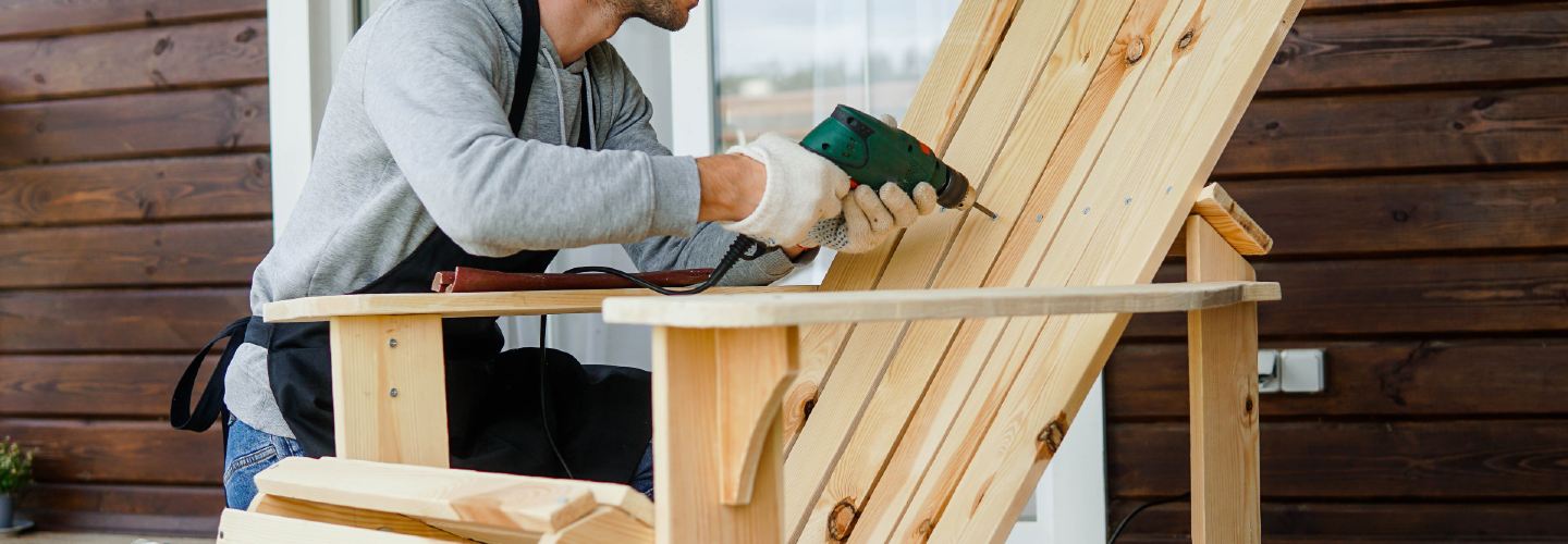 A person in workwear assembling outdoor furniture with the right tools such as a power drill.