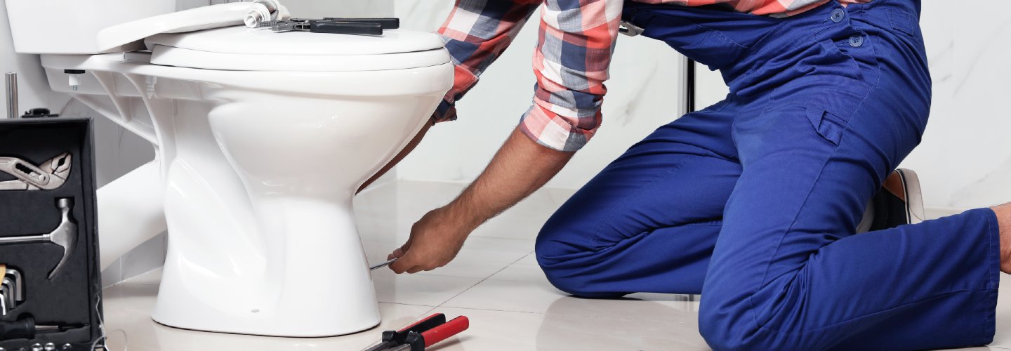 A plumber installing a new toilet in a bathroom, with tools and pipes visible.