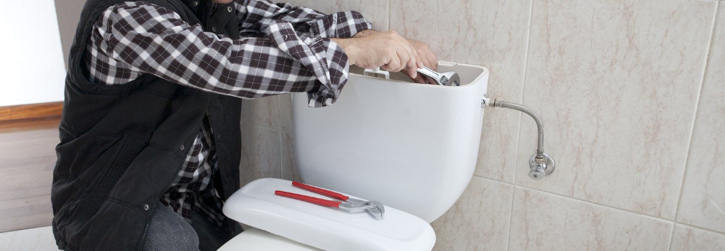 A plumber fixing a toilet with tools and parts scattered around, focused on repairing the flushing mechanism.