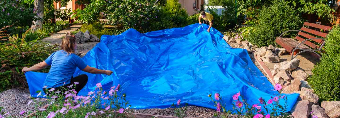 Two people laying on a blue tarp on a garden for pond installation
