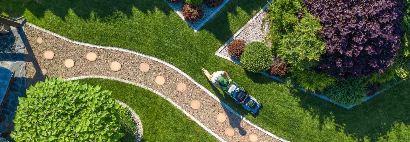 A landscape contractor working outdoors, wearing protective gear and using tools to shape and maintain a garden or outdoor space.