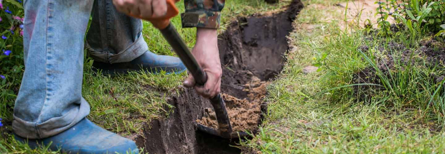 A person digging a trench with a shovel in a dirt field.