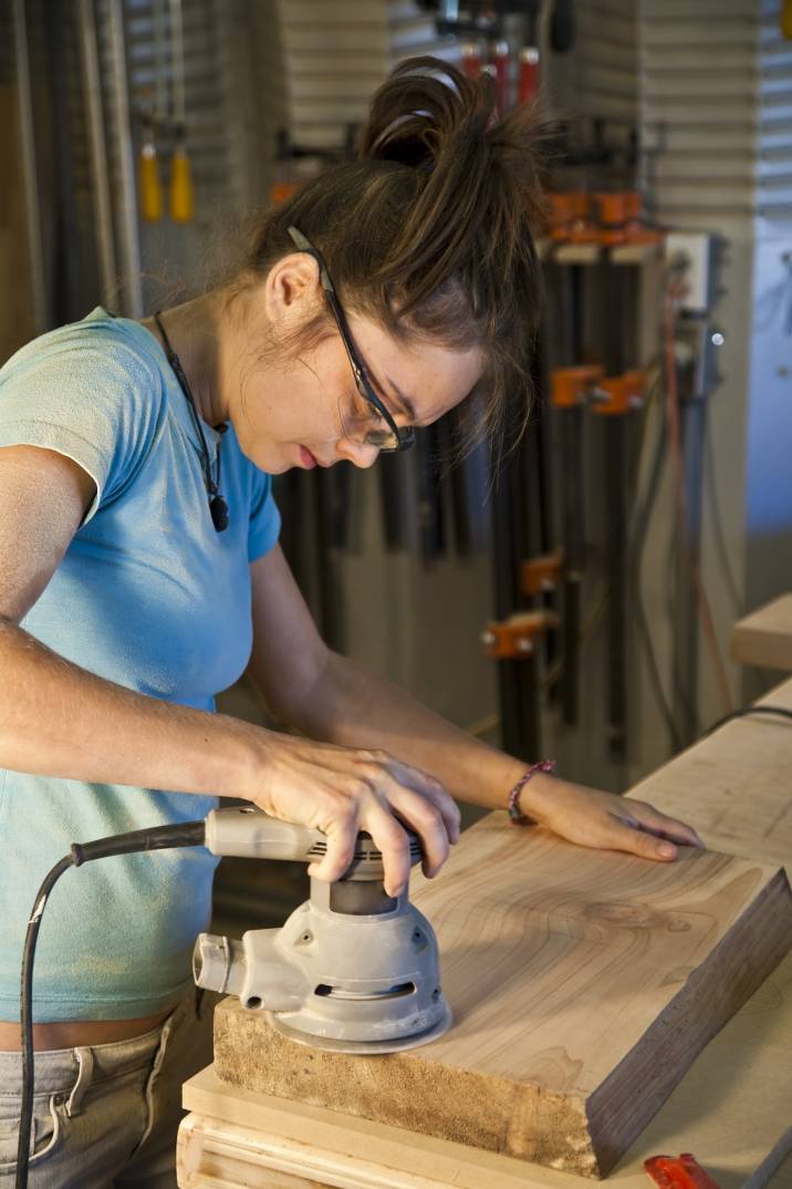 a young female apprentice sanding a cabinet part in a woodshop