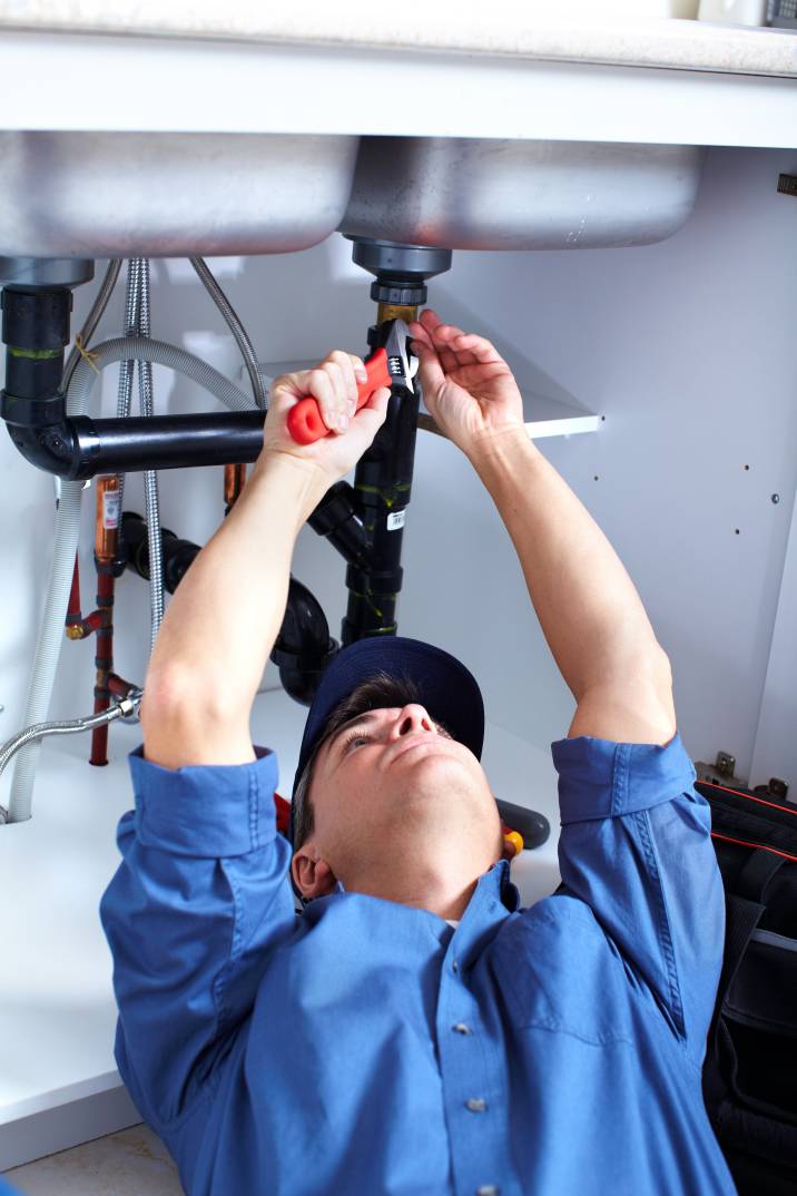 a man fixing black pipes underneath a sink