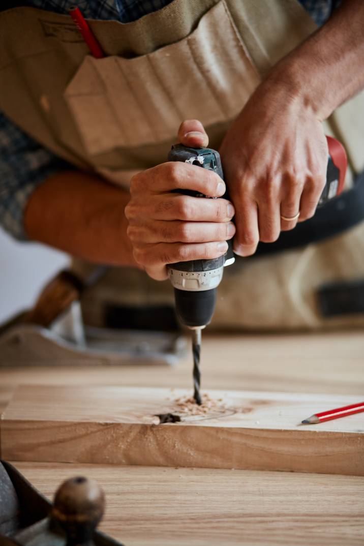 a carpenter drilling a hole in a thin plank of wood