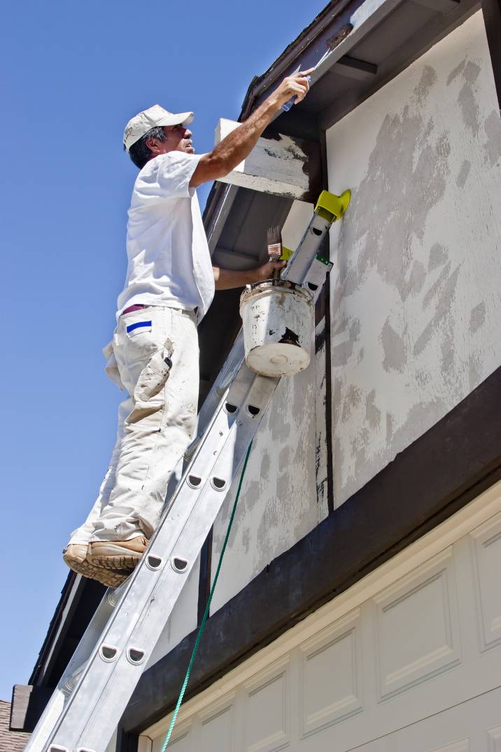 a uniformed man painting a house's gutters