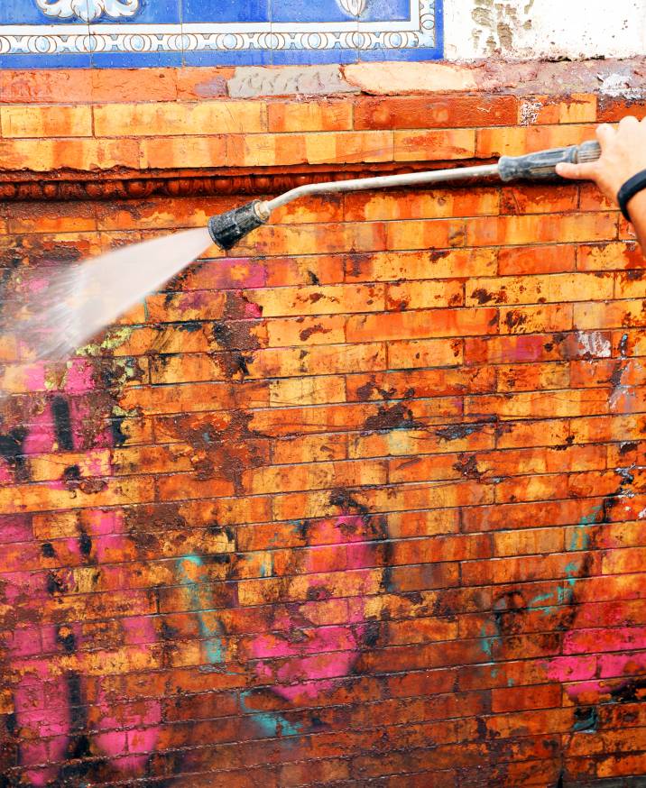 a man pressure washing a wall with graffiti
