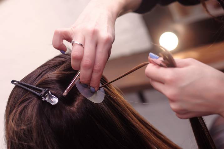 a woman getting hair extensions by a professional hairdresser