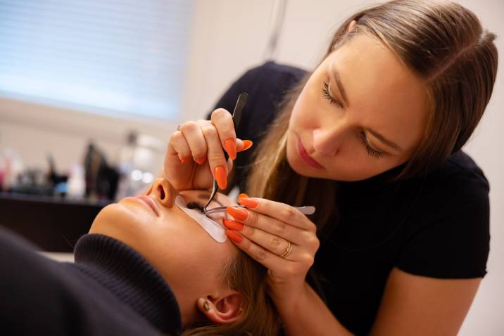 an eyelash technician using tweezers for eyelash extension procedure