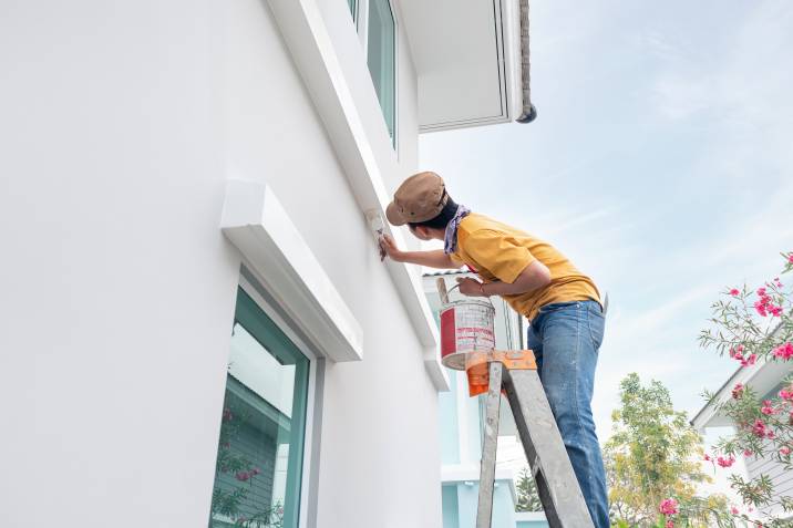 exterior painter stepping on ladder and painting a house