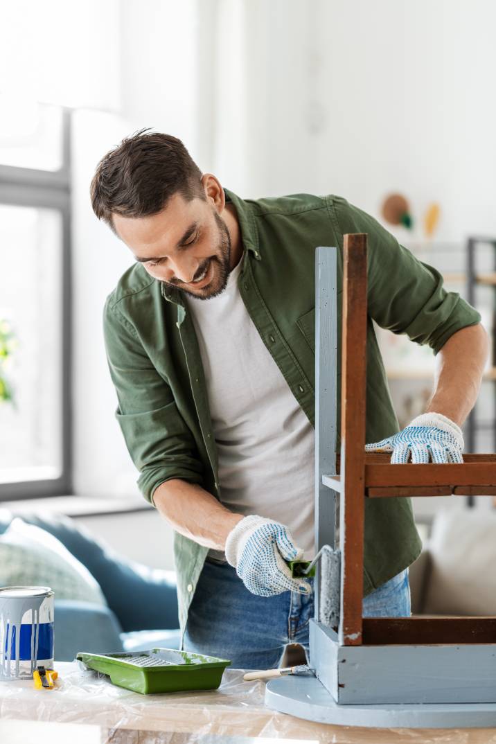 smiling male furniture painter, painting old wooden table indoors