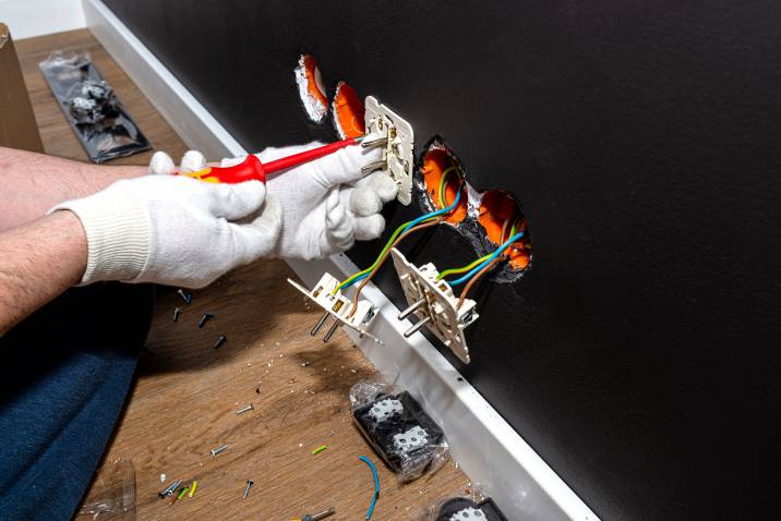 an electrician using a screwdriver to install new electrical socket