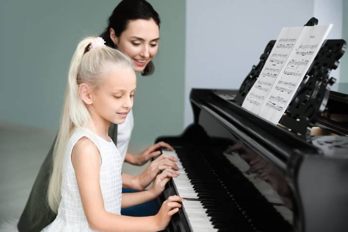 woman giving piano lessons to young girl