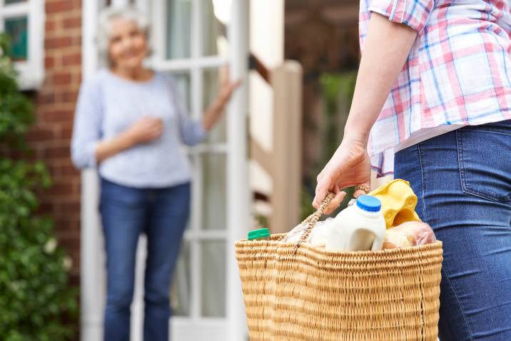 Person delivering basket of groceries to elderly woman