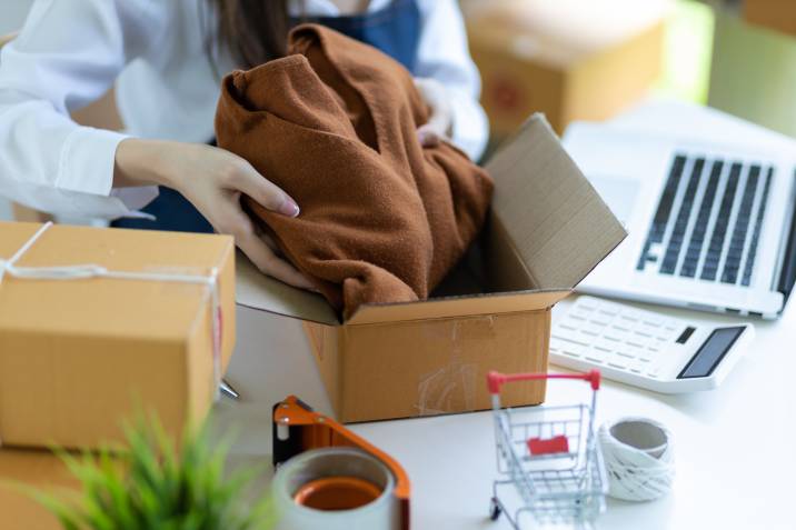 woman packing a sweater in delivery parcel, selling physical products on blog online store