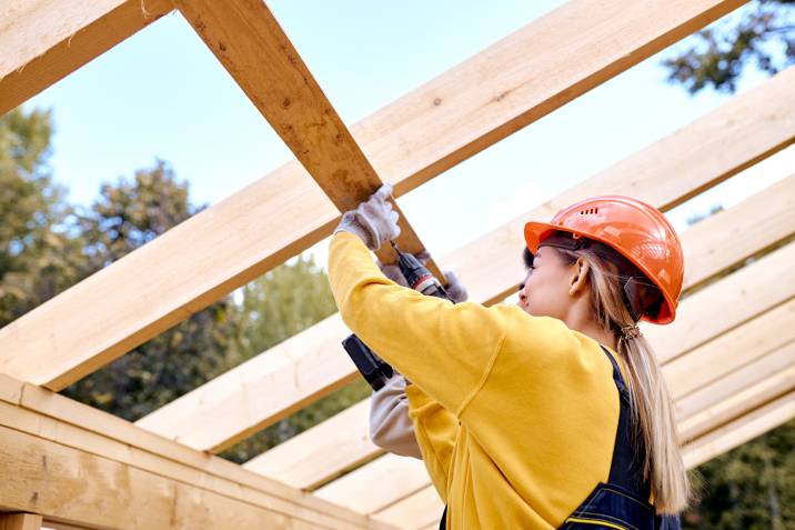 female carpenter working on roof section of wooden house skeleton frame