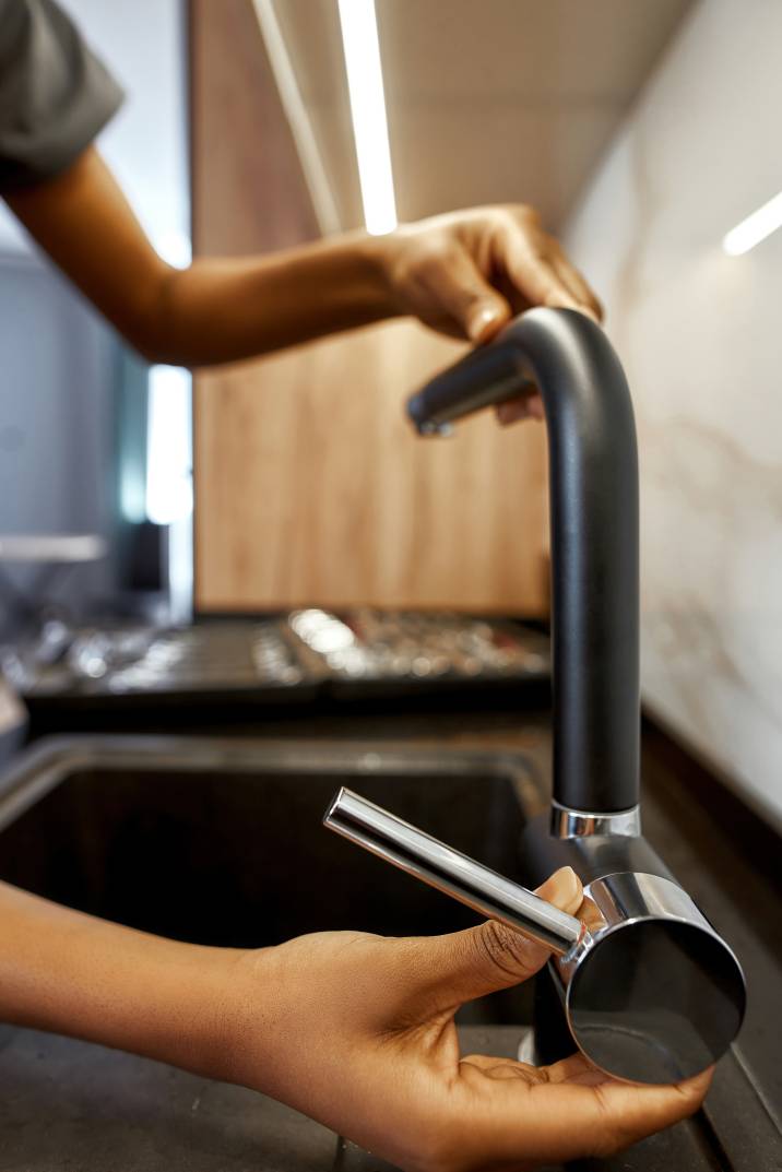 a handyperson installing a kitchen faucet with their hand on the tap handle