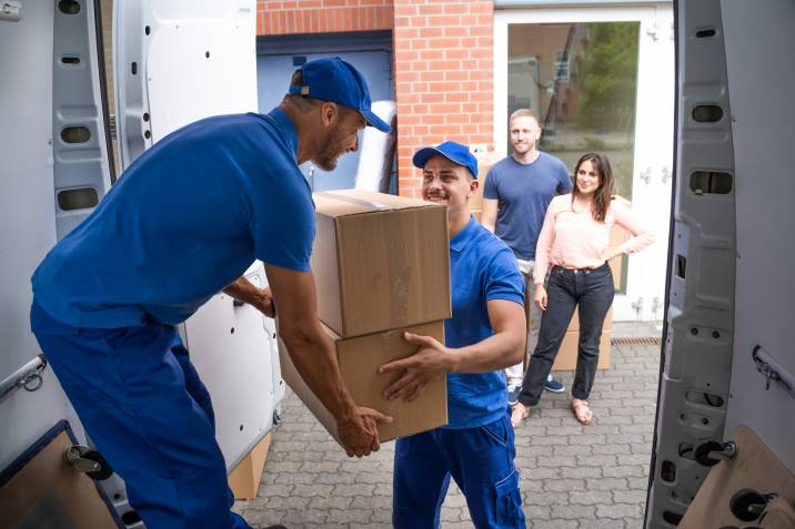movers helping each other carry moving boxes in front of a client