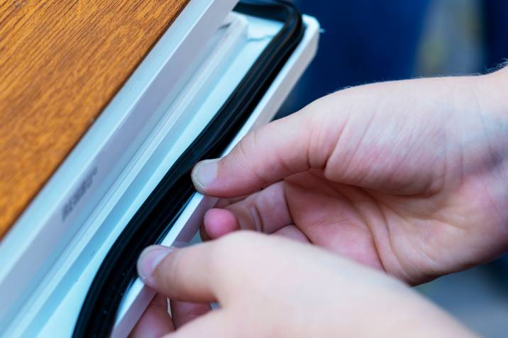 person fitting and measuring weatherstripping material on a window