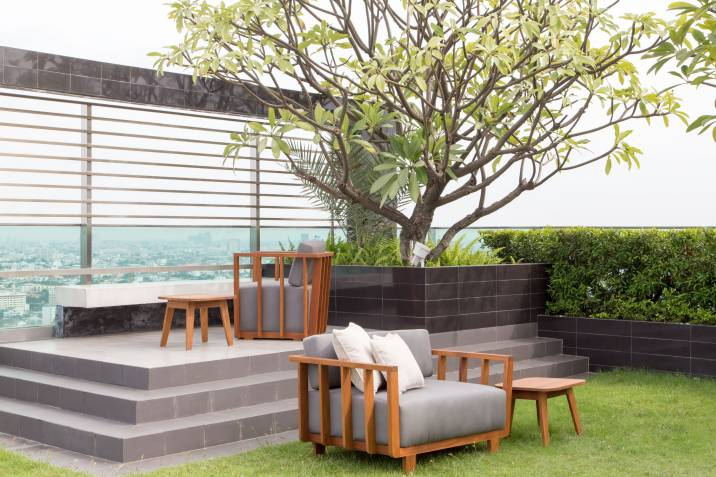 A modern garden design with wooden furniture, a small tree, and neatly arranged greenery on an elevated patio