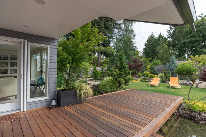 Modern wooden deck attached to a house, overlooking a landscaped garden with greenery and two orange lounge chairs on the lawn