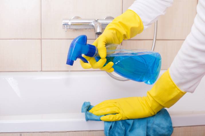 Spraying liquid detergent on bathtub, cleaning bathtub with cloth