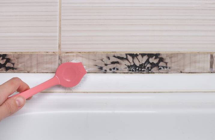 Brushing mold and mildew from tile joints around bathtub
