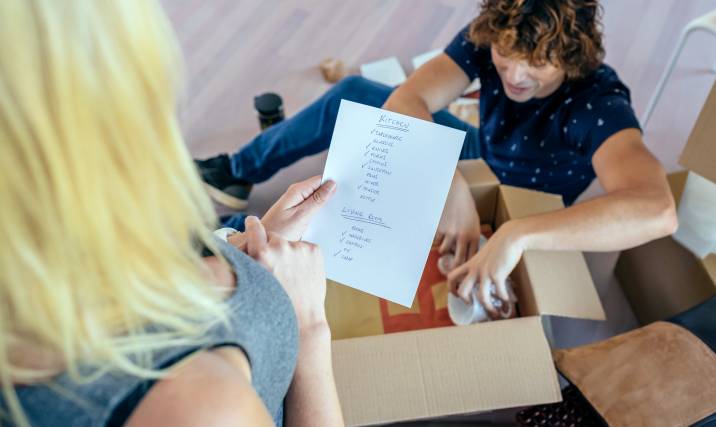 woman reading kitchen packing checklist while her partner packs items in boxes