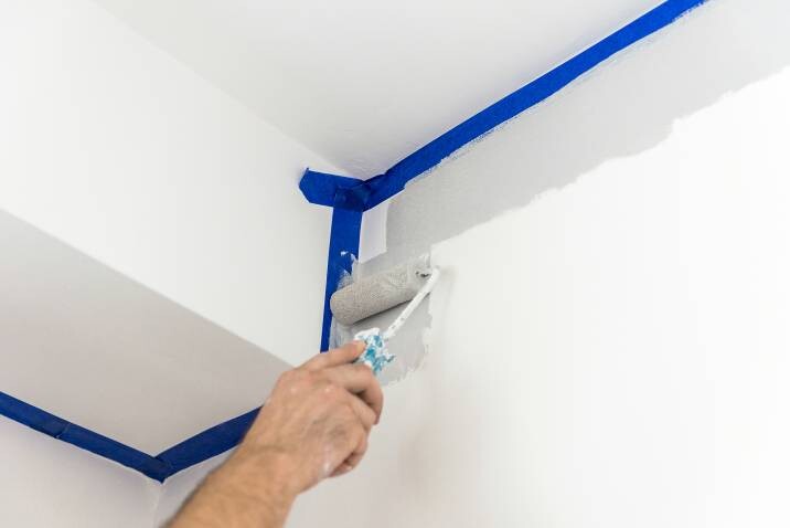 Closeup of hand painting wall with roller in gray color using blue painter’s tape