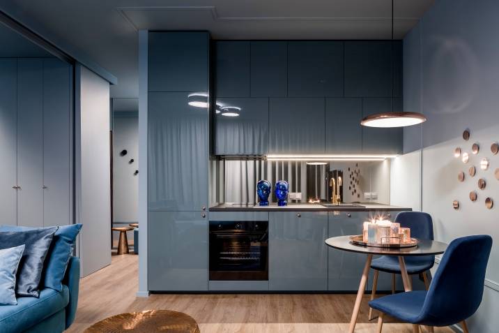 Dark home interior in blue with open kitchen and dining area with round table