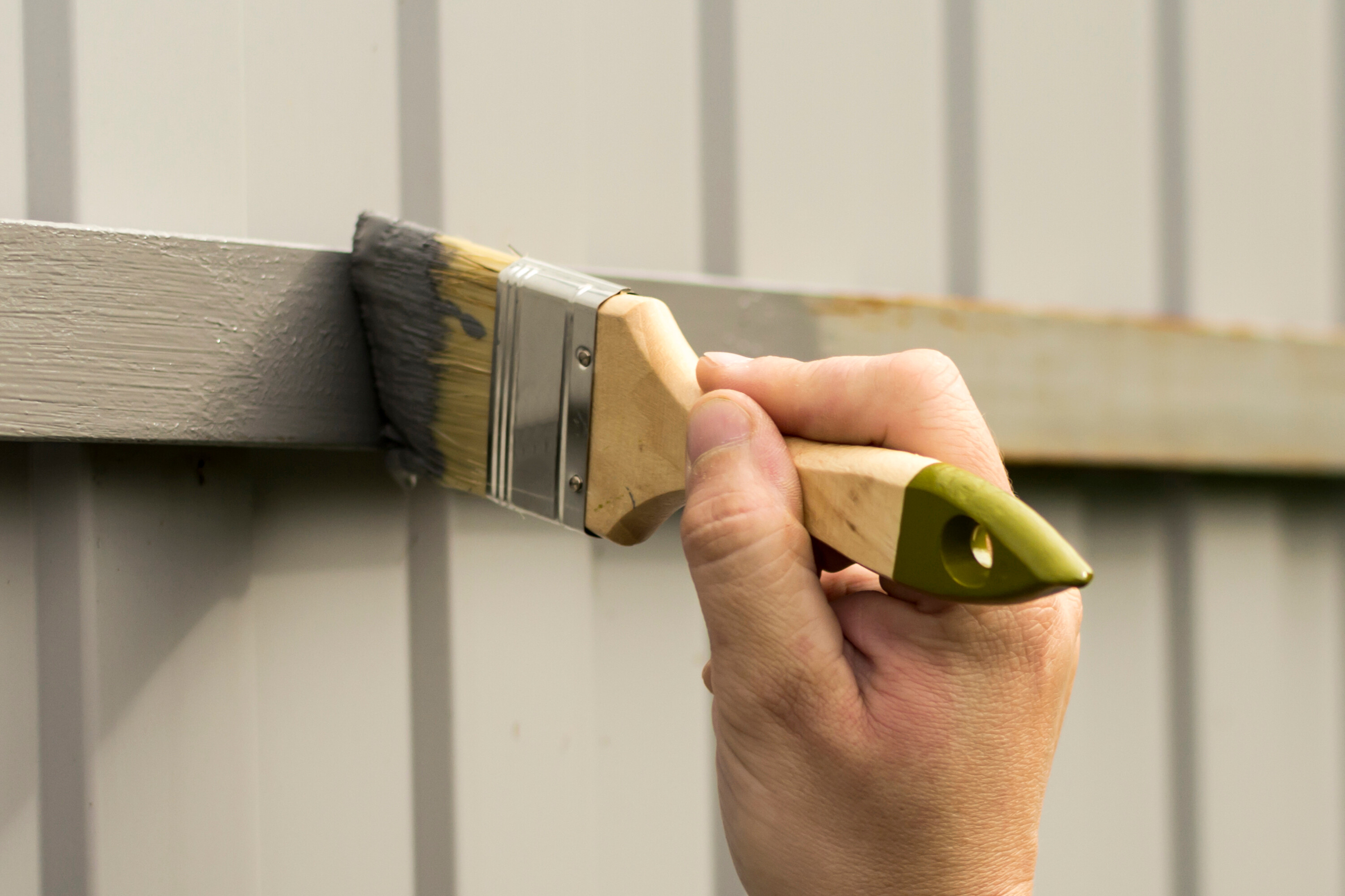 A close-up view of a fence being painted grey with a brush.
