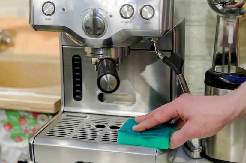 how to clean breville espresso machine - a man cleaning a espresso machine using a green sponge