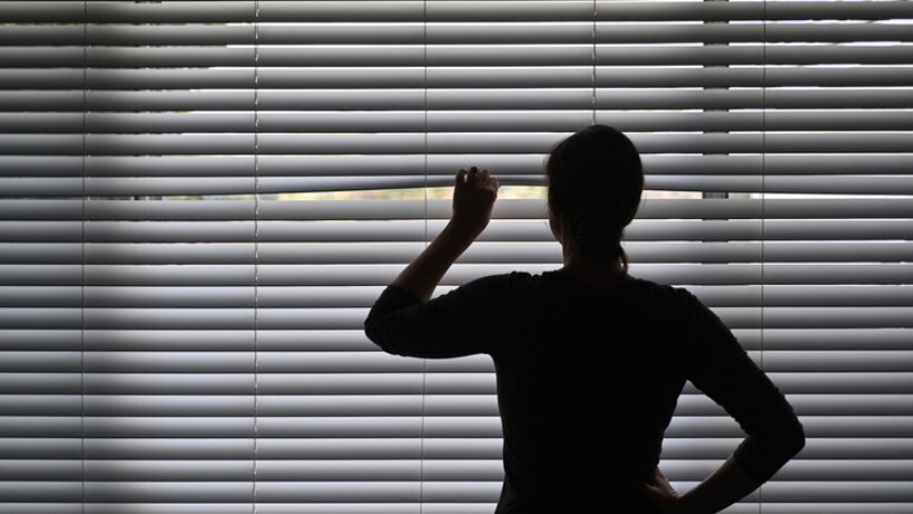 drapes vs curtains vs blinds - adult woman looking outside her home from her blinds, enjoying her privacy