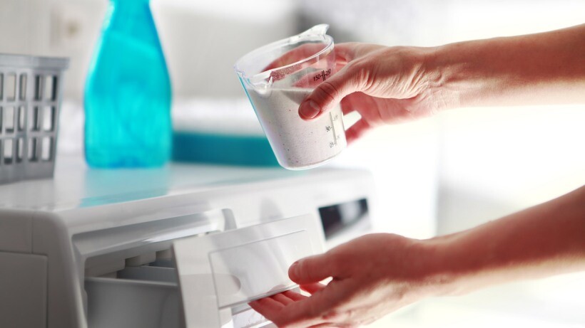 Fabric conditioner vs detergent - Hands of a person that fills detergent in the washing machine