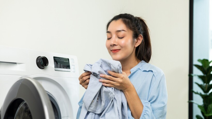 Fabric conditioner vs detergent - Woman smelling fragrant clean clothes washed from softener and washing machine.