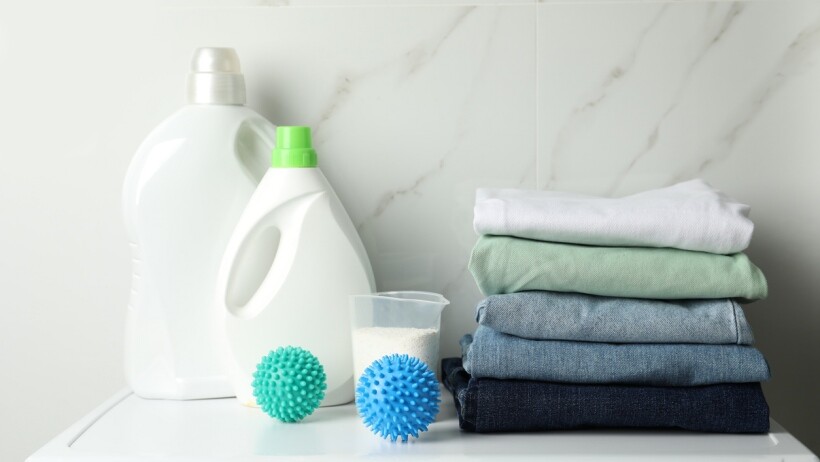 Fabric conditioner vs detergent - Stacked clean clothes and detergents on washing machine