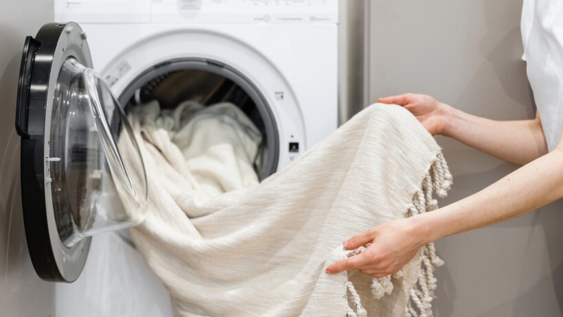 Fabric conditioner vs detergent - A woman unloading laundry from white washing machine