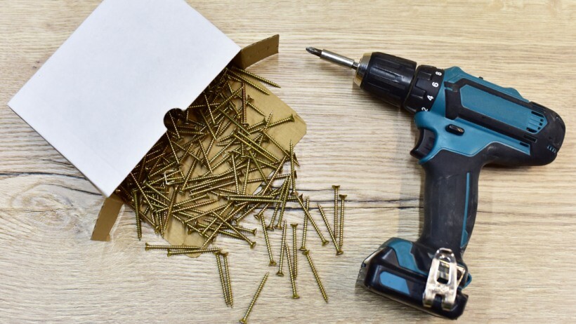 Impact driver vs drill - A cordless impact driver and self-tapping screws in a cardboard box on a wooden table