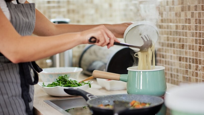 Gas vs electric range - A person in apron standing next to a range and preparing spaghetti