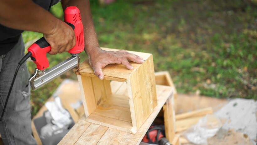 Nail gun vs staple gun - A handyperson shooting the nail by air nailer to a wooden square box